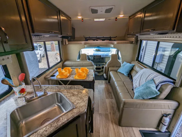 Spacious RV rental interior features kitchen with sink, dining area with bright yellow dishes, and comfy sofa.. Thor Four Winds 2020