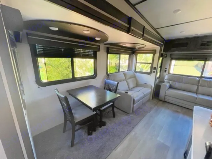 RV rental interior: A modern living space with a dining table, chairs, and two comfortable gray sofas by large windows.. Crossroads RV Cruiser Aire 2021