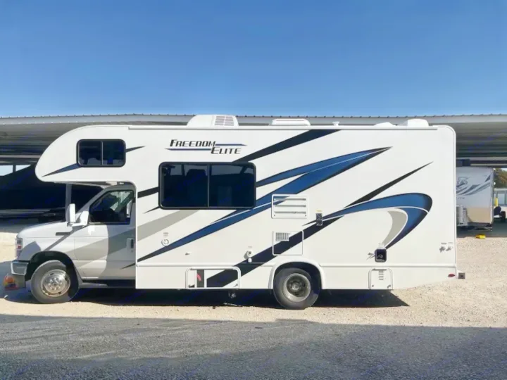 Side view of a white Freedom Elite Class C RV rental with blue graphics, parked in a sunny lot.. Thor Freedom Elite 2021