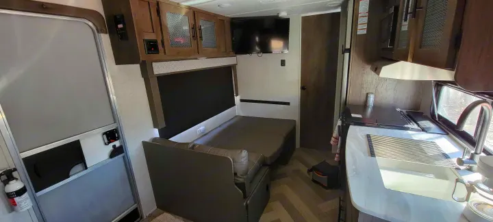 Modern RV rental interior showing a compact kitchen, convertible dinette/bed, TV, and entrance door for comfortable travel.. Forest River Wildwood X-Lite 2020
