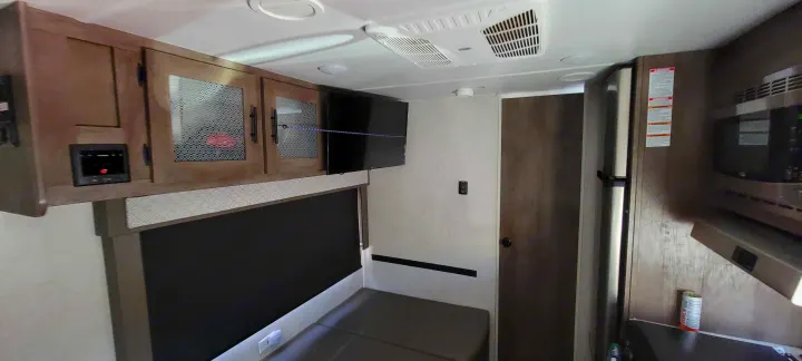 RV rental interior showing the compact living area. Features include wood cabinets, TV, kitchenette with microwave & fridge, and bench seating.. Forest River Wildwood X-Lite 2020