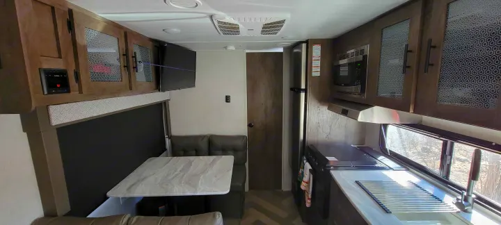 Inside this cozy **rv rental**: a compact kitchen with stove/microwave, dining table, and TV. Ideal for road trips!. Forest River Wildwood X-Lite 2020