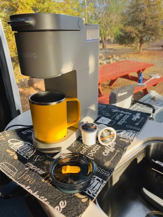 Enjoying fresh coffee in an RV rental. A Keurig brewer with a yellow travel mug and Peet's K-cups sits on a coffee mat.. Pleasure Way Lexor 2017