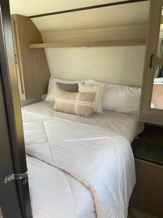 RV rental bedroom: a comfy bed with decorative pillows, overhead shelf, and compact storage areas. Ready for your next journey.. Keystone RV Hideout 2021