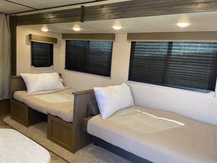 Cozy RV rental interior featuring two twin beds, white pillows, and windows with dark blinds for a restful sleep.. Keystone RV Hideout 2021