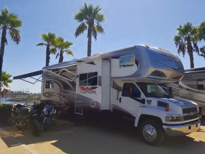 Spacious Road Warrior RV rental, a motorhome with motorcycles, parked by the bay under palm trees, ready for travel.. Weekend Warrior Weekend Warrior Motorhome 2009
