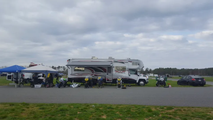 A large RV, possibly an **rv rental**, serves as base camp at a track day, surrounded by race bikes, gear, and tents under a cloudy sky.. Weekend Warrior Weekend Warrior Motorhome 2009