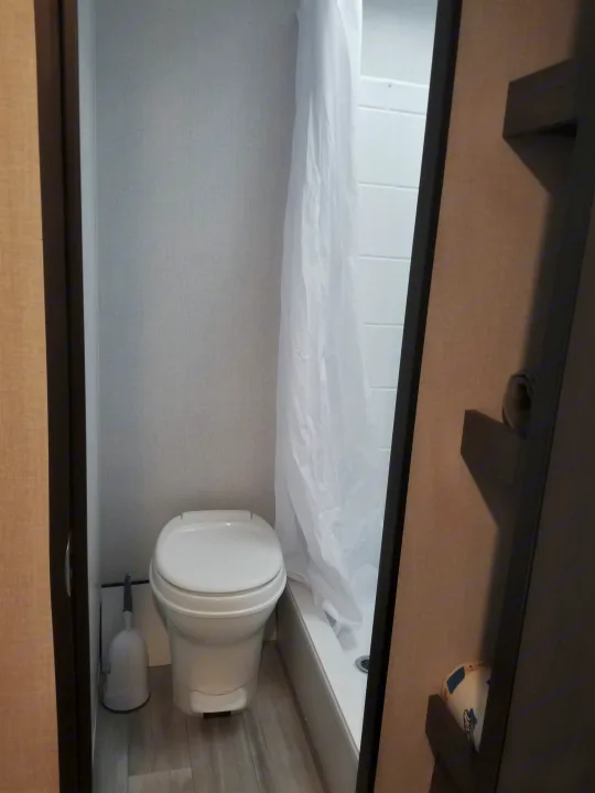 Compact RV rental bathroom: features a white toilet, toilet brush, and shower stall with a white curtain.. Coachmen Clipper 2022