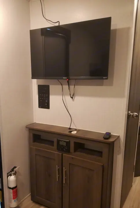 An RV rental interior showing a mounted Roku TV, control panel, entertainment unit, and fire extinguisher.. Coachmen Clipper 2022