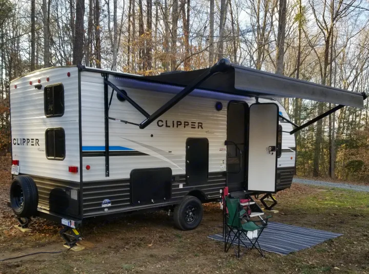 Clipper travel trailer (RV rental) set up for camping in a wooded area with an extended awning and outdoor living space.. Coachmen Clipper 2022