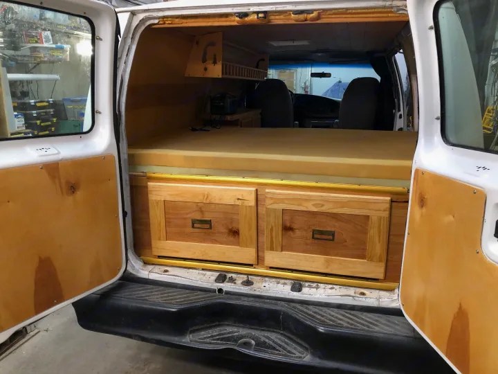 This RV rental camper van features a custom wood interior with a bed, drawers, and overhead storage, ready for adventure.. Ford E250 Camper Van 2001