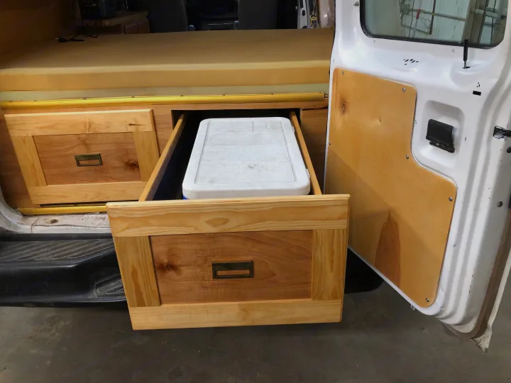 RV rental custom storage: wood drawers with a cooler inside a camper van. Foam bed & open door.. Ford E250 Camper Van 2001