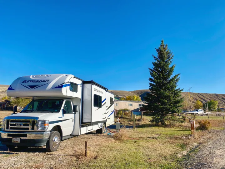 White Sunseeker RV rental parked at campsite 61 with hookups, a tree, and hills under a clear blue sky.. Forest River Sunseeker 3250DSLE 2022