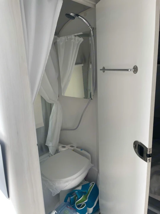 Compact RV rental bathroom featuring a shower, toilet, and a towel bar on the right wall.. Airstream Bambi 2021