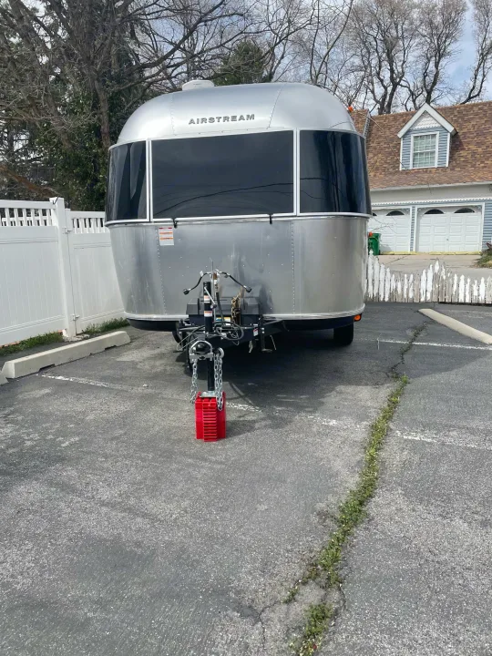Silver Airstream travel trailer parked on red blocks on an asphalt lot. Explore RV rental options!. Airstream Bambi 2021