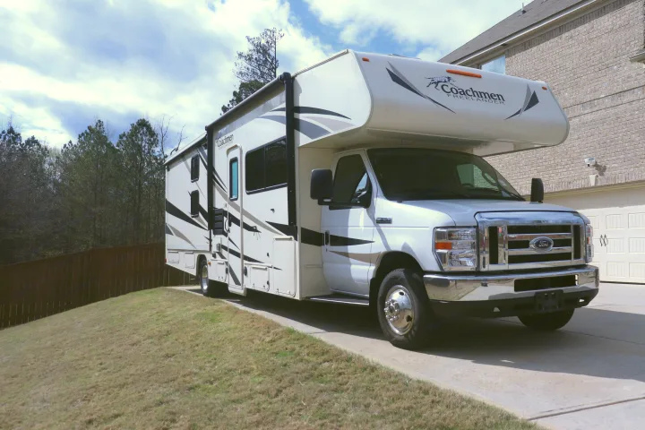 White Coachmen Freelander RV rental parked on a driveway beside a house and trees.. Coachmen Freelander 2020