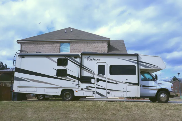 A white Coachmen Freelander Class C rv rental, with black & grey graphics, parked by a brick house for travel.. Coachmen Freelander 2020
