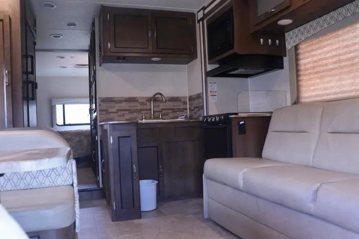 This rv rental offers a well-appointed kitchen area with stove, sink, and microwave, alongside comfy dinette and sofa seating.. Coachmen Freelander 2020