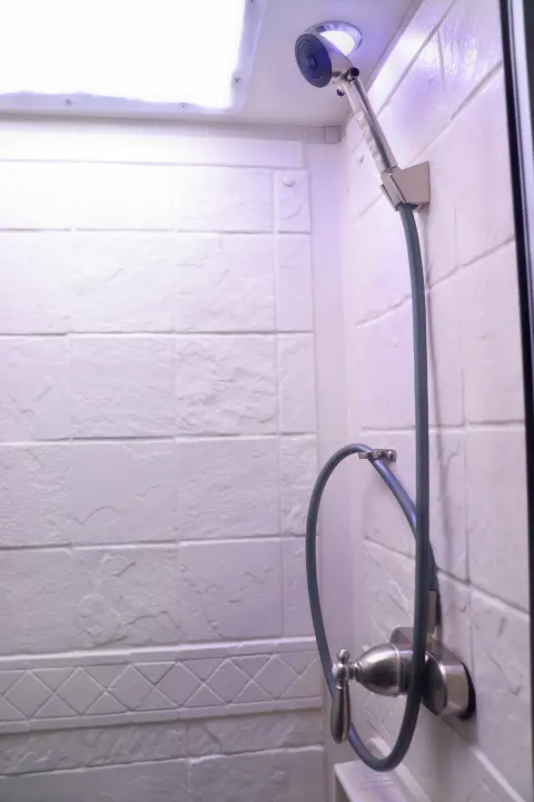 Compact, well-lit shower in an RV rental, featuring a handheld showerhead & textured white tiles. Perfect for travel!. Coachmen Freelander 2020