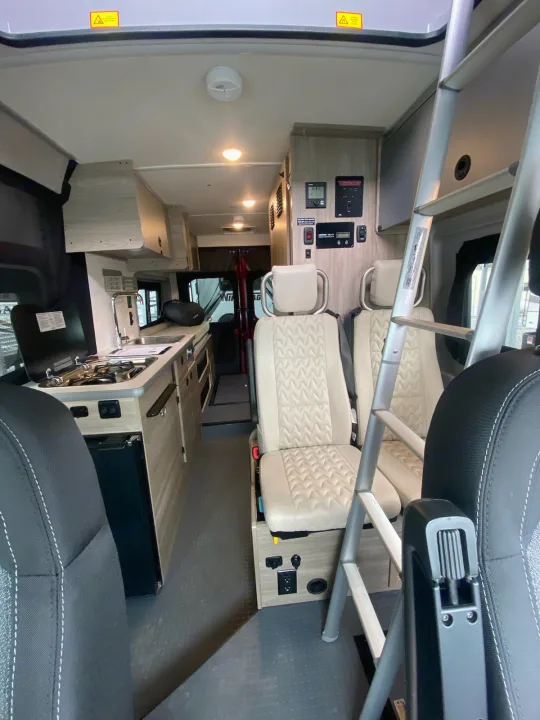 Interior of an RV rental, featuring a compact kitchenette, ladder to bunk, and comfortable seating. Ready for adventures!. Winnebago Solis 2022