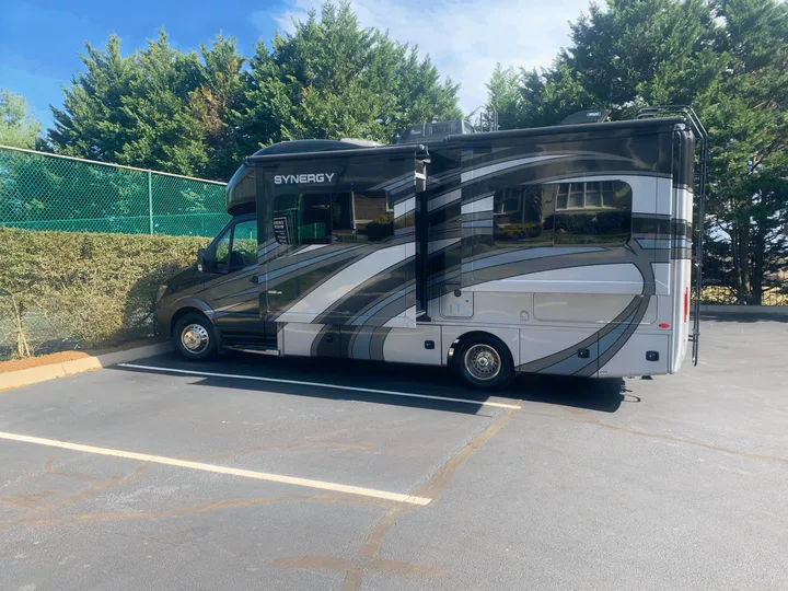 A sleek black and grey Synergy motorhome, likely an rv rental, is parked with its slide-out extended in a lot.. Thor Synergy 2018