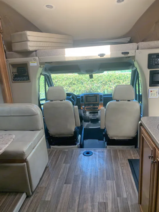 Inside an RV rental: front view showing driver/passenger seats, overhead bunk, dinette, and modern flooring.. Thor Synergy 2018