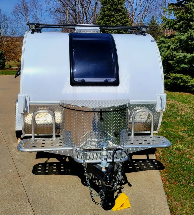 This white teardrop RV rental is parked outdoors, featuring a diamond plate storage box and roof rack with lights.. nuCamp T@G 2020