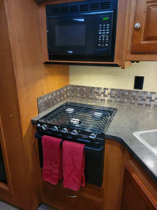 Compact RV rental kitchen featuring a High Pointe microwave, Wedgewood Vision stove, sink, and tiled backsplash. Perfect for travel.. Winnebago Vista 2018