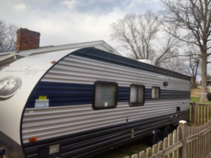 Grey and blue travel trailer, resembling an RV rental, with multiple windows, parked by a house and fence on a cloudy day.. Forest River Cherokee Grey Wolf Special Edition 2021