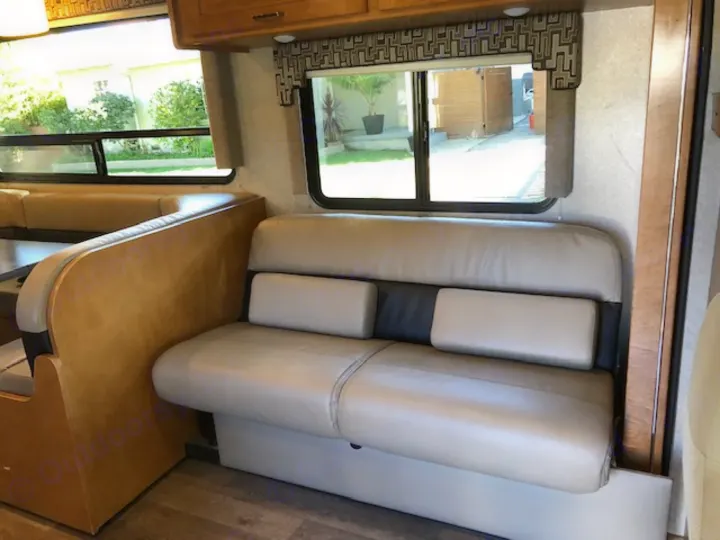 Inside an RV rental: a light-colored dinette booth on the left and a sofa with pillows on the right, by windows.. Winnebago Minnie Winnie 2019