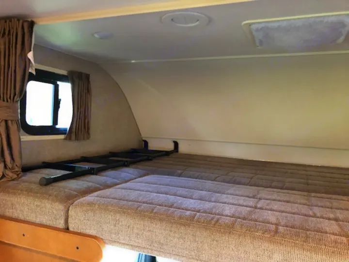 Interior view of an RV rental's cab-over bunk, featuring a comfortable mattress, folded ladder, and window.. Winnebago Minnie Winnie 2019