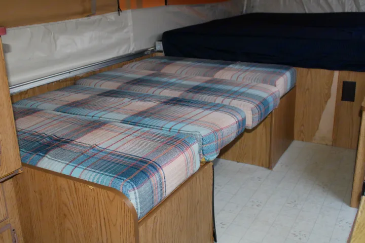 RV rental interior with plaid seating/bed area, a separate bed, and wood-paneled walls.. Coleman Destiny Royale 1992