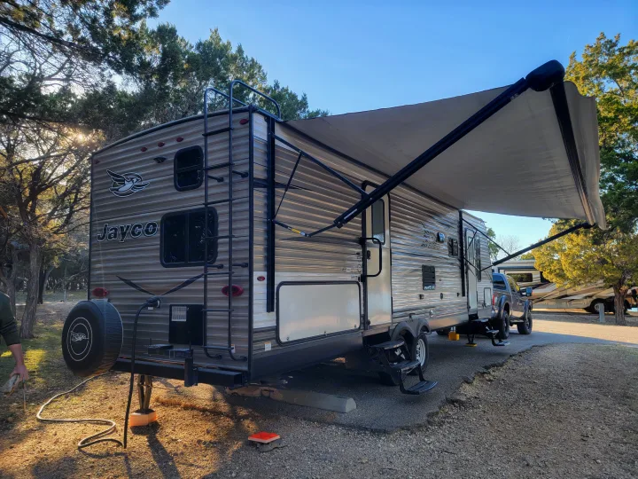 A Jayco travel trailer rv rental, fully set up at a sunny campsite, awning extended for shade.. Jayco Jay Flight 2018