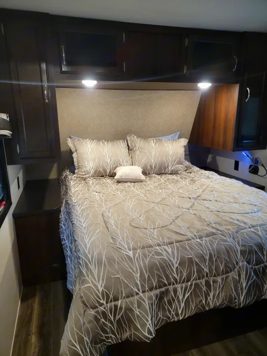 RV rental bedroom: a well-lit, cozy space with a large bed, patterned bedding, and dark wood overhead cabinets.. Jayco Jay Flight 2018