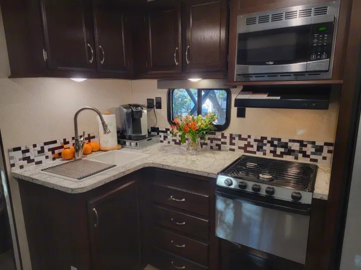 Modern RV kitchen interior, perfect for an RV rental. Features dark wood cabinets, sink, microwave, stove, and contemporary backsplash.. Jayco Jay Flight 2018
