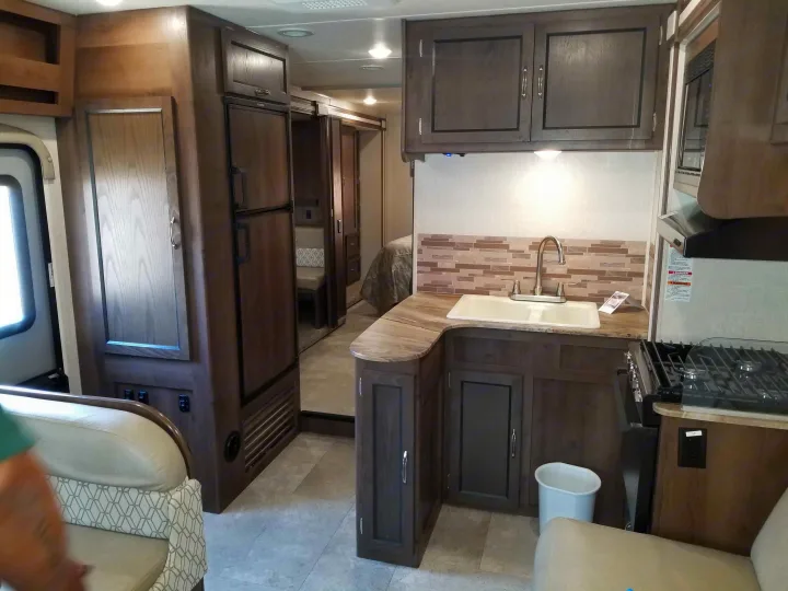 Interior of an **rv rental**: kitchen with sink, stove, microwave, and wood cabinets. Leads to living area and bedroom.. Coachmen Freelander 2020