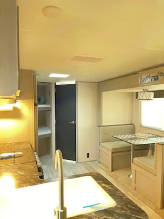 Interior of a modern RV rental, featuring a kitchen sink in the foreground, a dinette booth, and bunk beds.. Forest River Tracer 2022