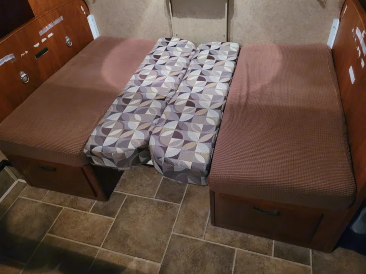 Cozy RV rental interior: a convertible dinette bed with brown seat cushions, patterned backrests, and convenient storage below.. Forest River Sunseeker 2013