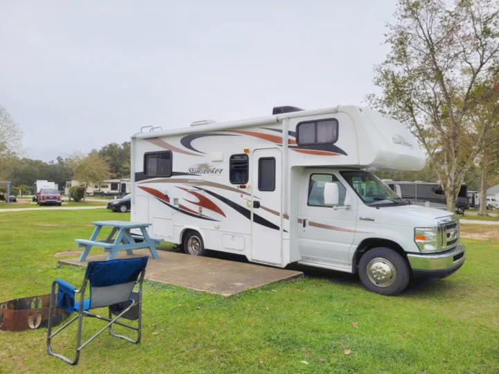 An RV rental parked on a concrete pad at a grassy campsite with a picnic table, chair, and fire pit.. Forest River Sunseeker 2013
