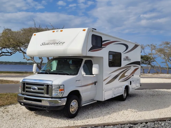 Explore with this white Sunseeker RV rental, a Class C motorhome parked on a gravel lot by the water.. Forest River Sunseeker 2013