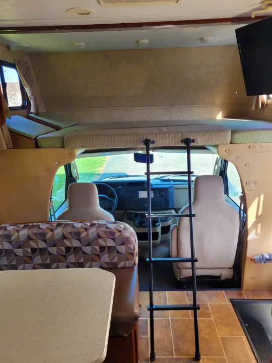 Interior view of an RV rental, showing the cab, overhead bunk with ladder, and dining area.. Forest River Sunseeker 2013