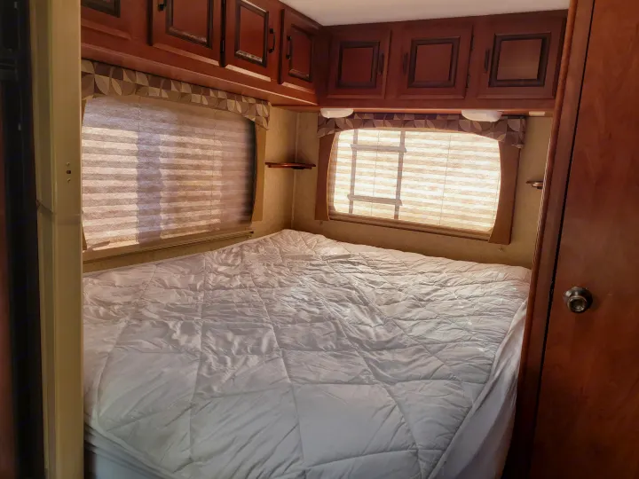 Comfortable RV rental bedroom with a large bed, windows, and overhead cabinets for your next road trip.. Forest River Sunseeker 2013