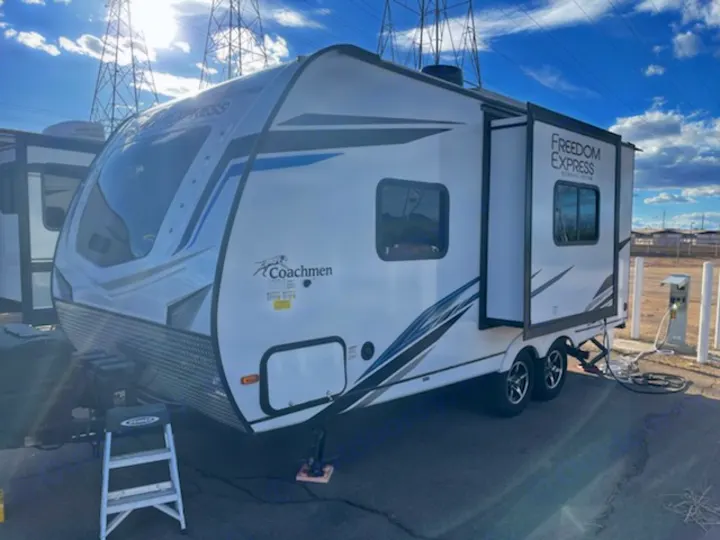 A modern white Coachmen Freedom Express RV, perfect for rv rental, parked outdoors with a slide-out open under power lines.. Coachmen Freedom Express 2022