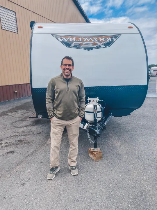 Excited man poses with his Wildwood FSX travel trailer, featuring propane tanks. Ideal for your next rv rental trip!. Forest River Other 2022