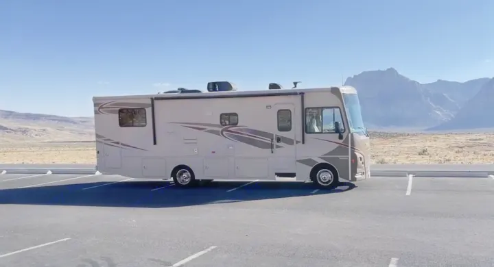 A tan rv rental is parked in a desert landscape with rugged mountains under a clear blue sky.. Winnebago Vista 2016