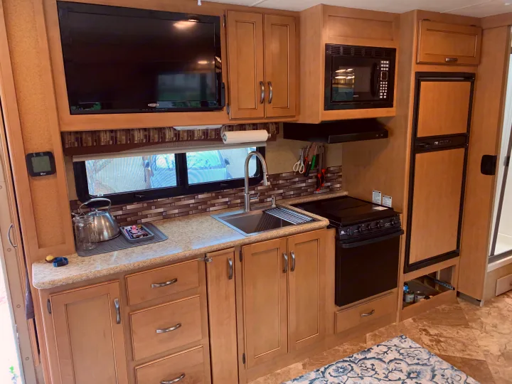 Compact RV rental kitchen with light wood cabinets, TV, microwave, sink, and stove, showcasing functional design for travel.. Other A.C.E 2016