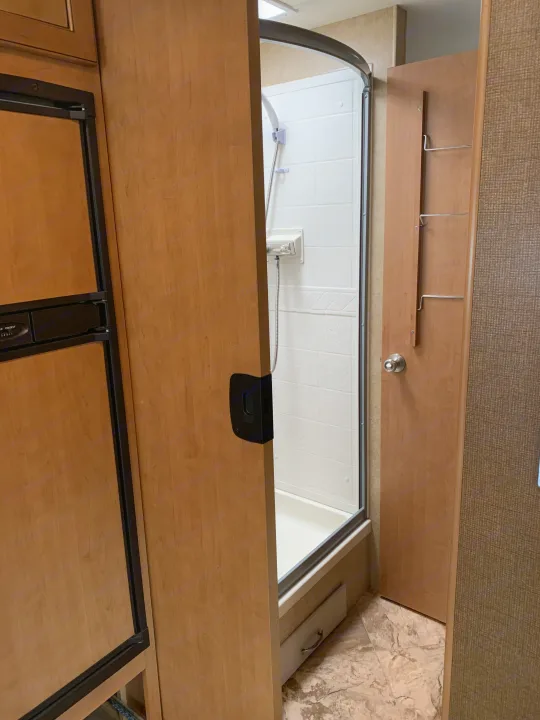 Inside an RV rental: a compact living space with a refrigerator, a shower stall, and a bathroom door with storage.. Other A.C.E 2016