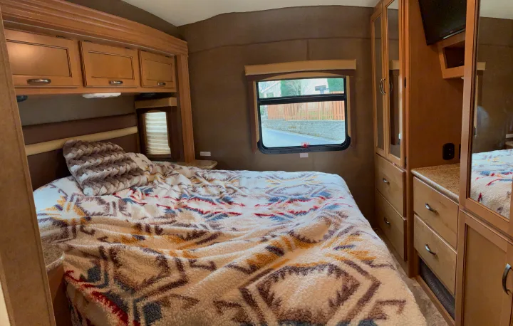 Cozy RV rental bedroom with patterned bedspread, overhead cabinets, window view, and mirrored closet storage.. Other A.C.E 2016
