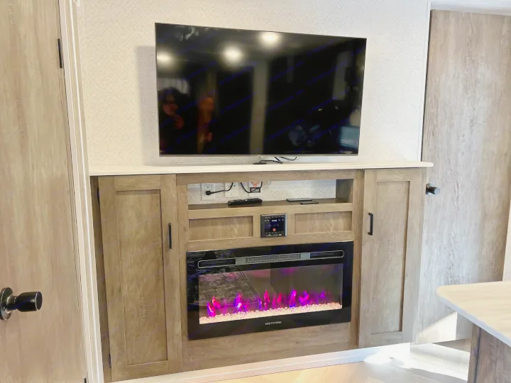 This RV rental features a cozy entertainment center with a TV, wood console, and a vibrant electric fireplace.. Forest River Other 2022