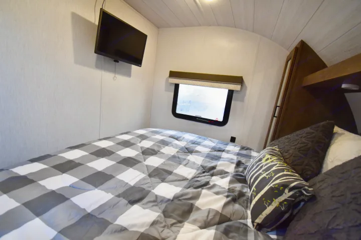 Cozy RV rental bedroom showing a checkered bed, wall-mounted TV, and window with a blind.. Forest River Other 2022